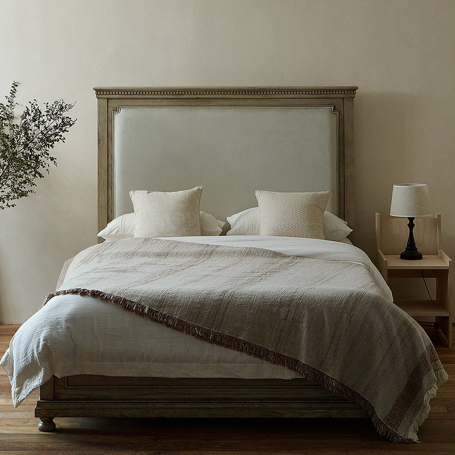 Massive wooden bed with upright slatted headboard and natural linen bedding