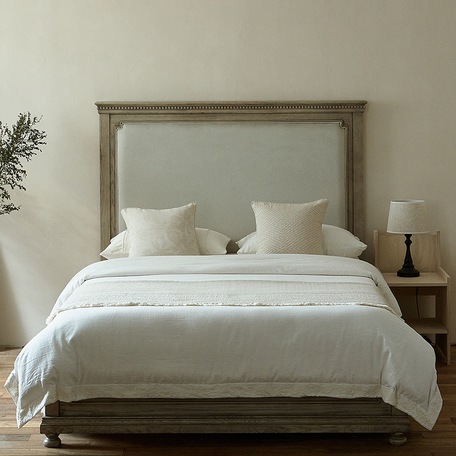 Massive wooden bed with upright slatted headboard and natural linen bedding