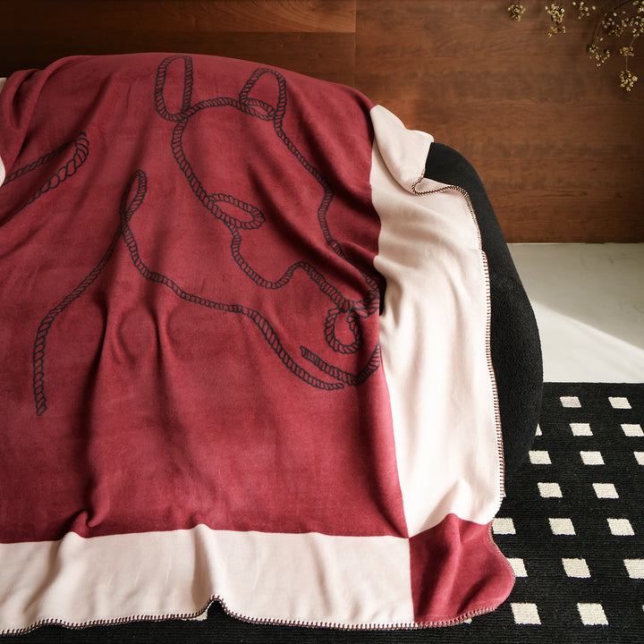 Throw blanket with embroidered cord motif and decorative stitching