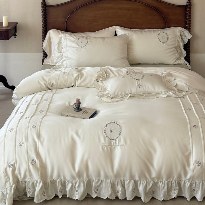 Satin bedding set with embroidered wreath motif, ruffled hem and decorative piping
