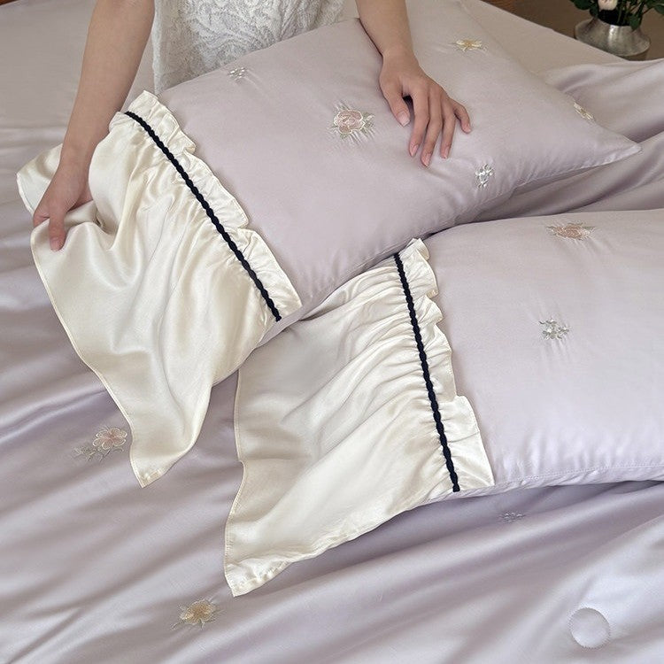 Exquisite satin bedding set with floral embroidery, gathered pillow shams, and contrasting piping