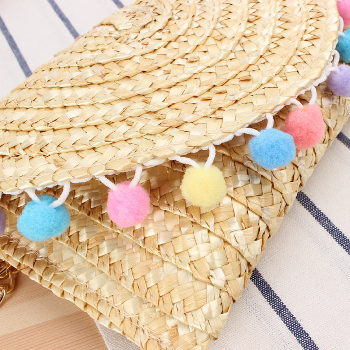 Clutch made of handwoven natural material with decorative pompons Stornfield