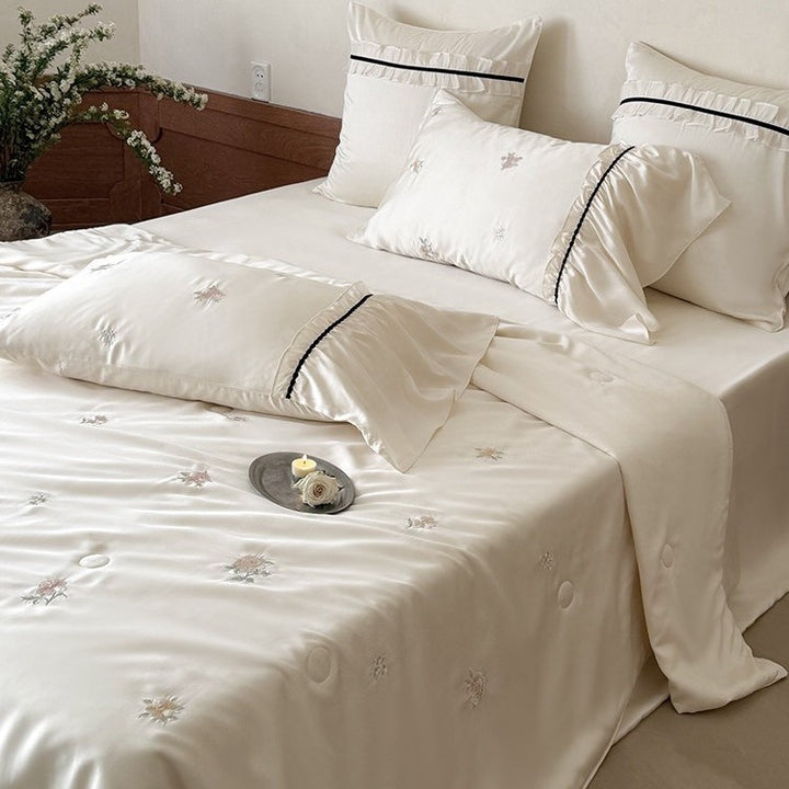 Exquisite satin bedding set with floral embroidery, gathered pillow shams, and contrasting piping