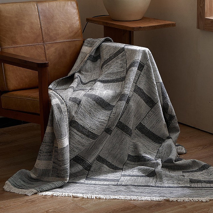 Large cozy living blanket made of cotton blend fabric with geometric jacquard pattern and fringed hem